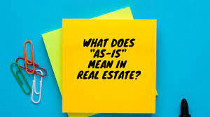 A bright yellow sticky note with bold black text reading "What Does 'As-Is' Mean in Real Estate?" placed on a blue background with colourful paperclips, representing the theme of a blog exploring real estate terminology.